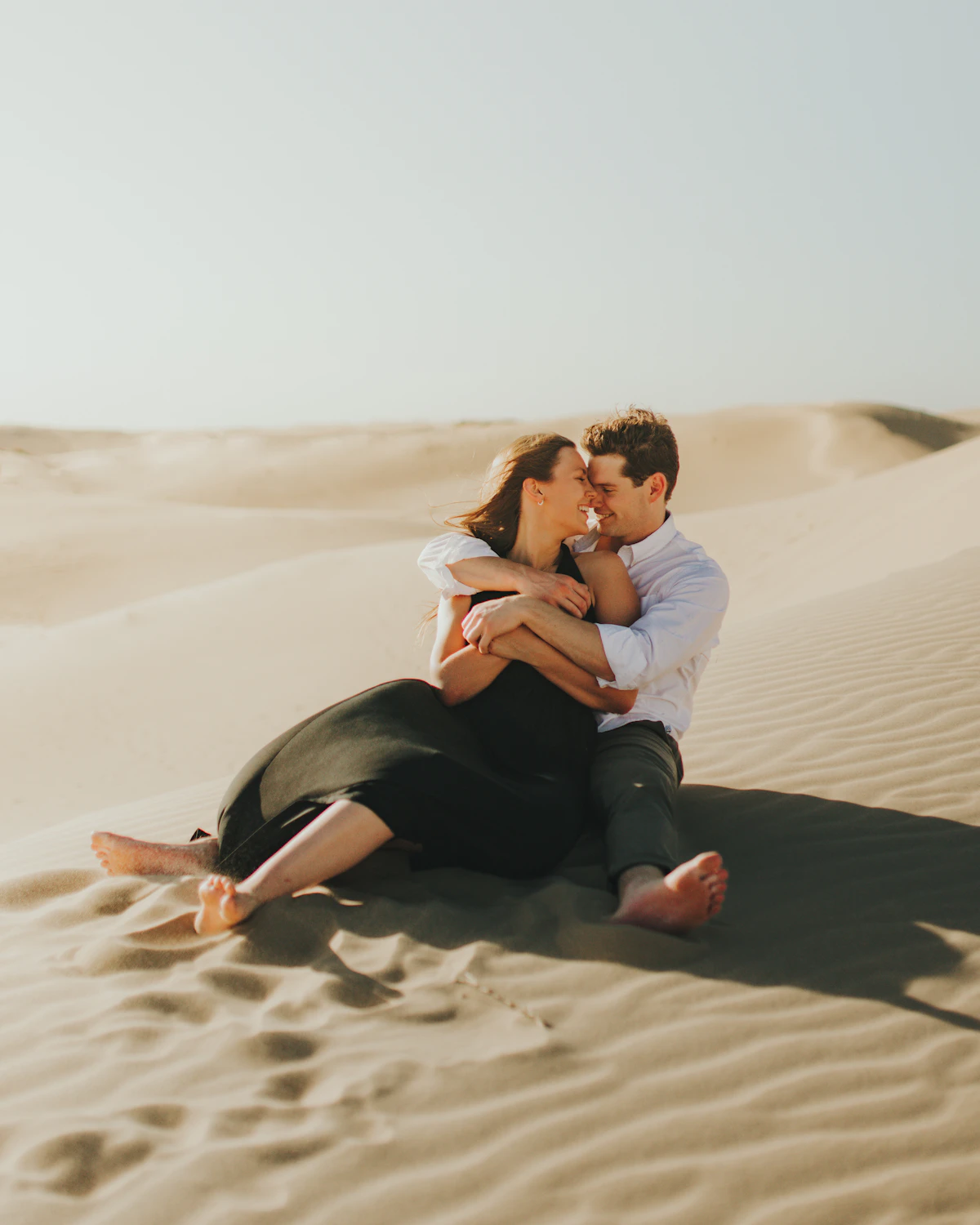 An engaged couple embracing on a sand dune