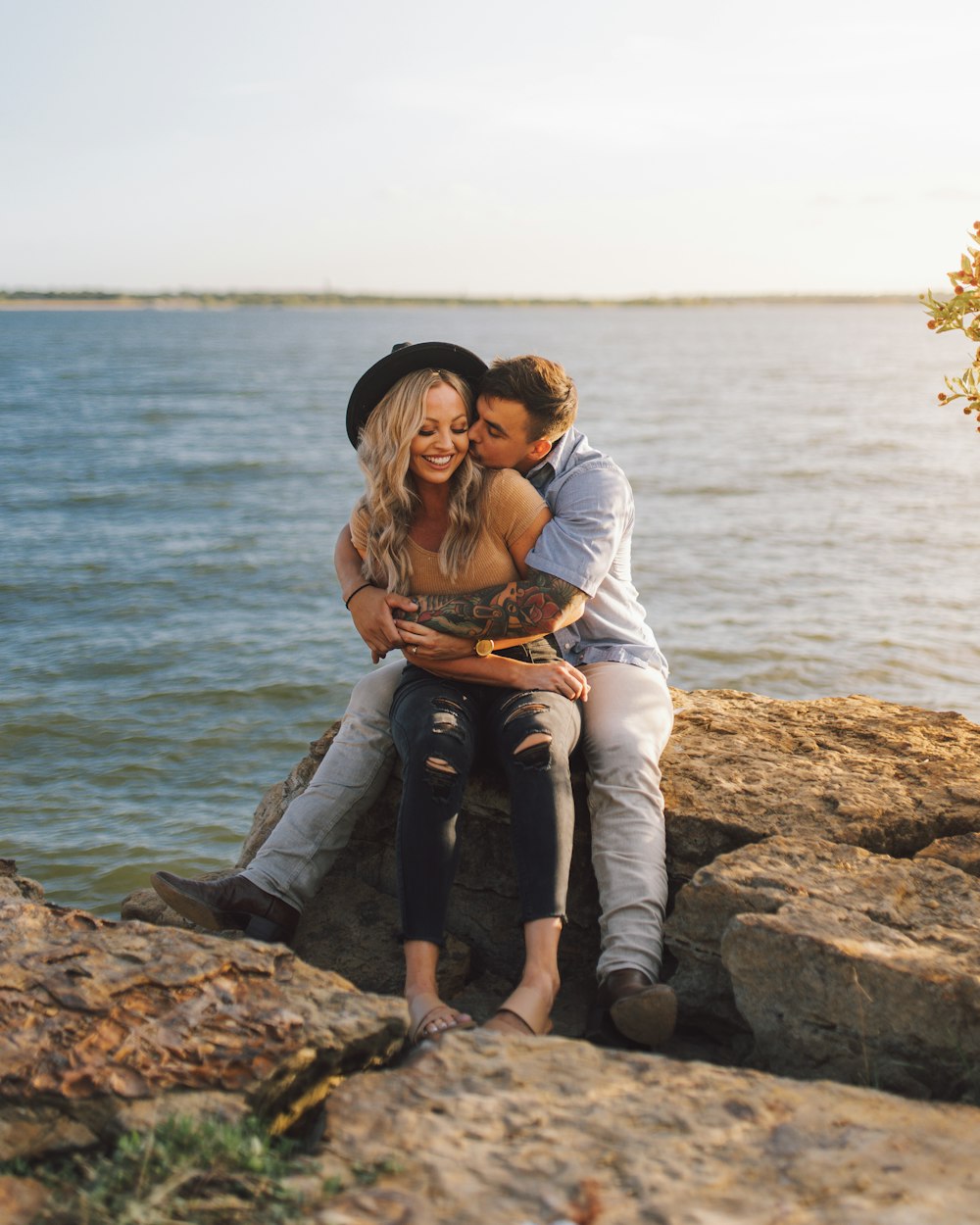 a man and woman sitting on a rock by the water