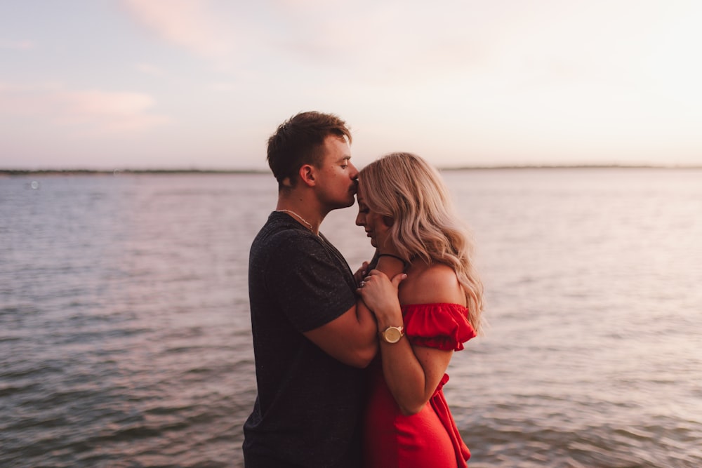 a man and woman kissing in front of a body of water