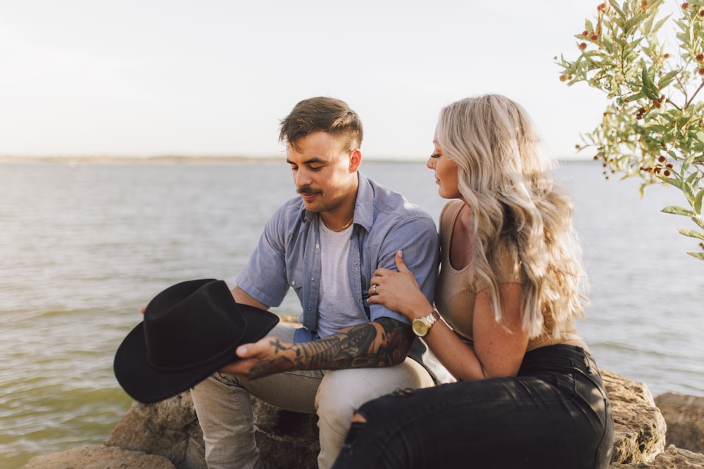 a man and woman sitting on a rock by the water