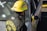 A firefighter, wearing a yellow helmet and a black fire jacket with the words 'SNOHOMISH FIRE' on the back, is standing next to a silver car. The car has yellow caution tape around its side mirror and appears to have been involved in an incident.