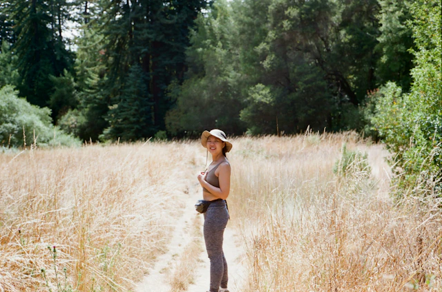 A sunlit trail with a person wearing a wide-brimmed outdoor hat, surrounded by nature.