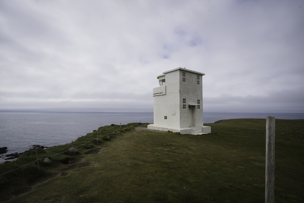 a white tower on a grassy hill by the water with Beachy Head in the background