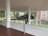 A vintage airplane is suspended within a modern architectural space, featuring large windows and white pillars. The plane has a grey body with black and white markings, and a wooden propeller at the front. The background shows a lush green landscape through glass.