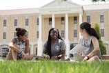 a group of women sitting on the grass in front of a building