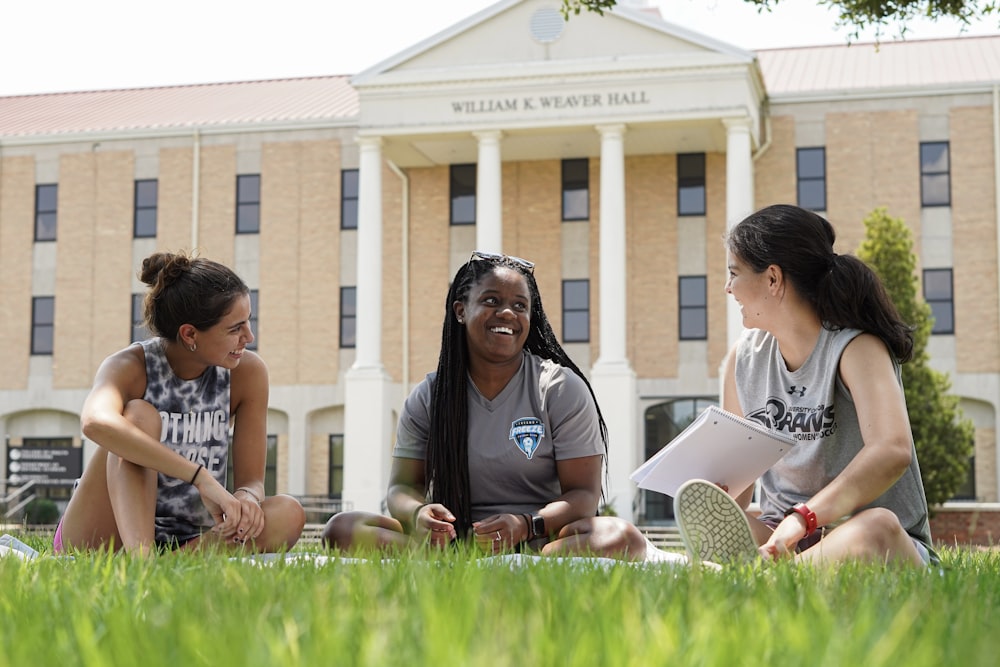 a group of women sitting on the grass in front of a building