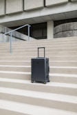 A sleek black rolling suitcase standing upright on a city sidewalk.