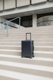 A sleek, modern rolling suitcase standing beside a travel backpack on a city sidewalk.