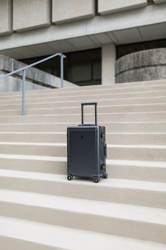 A sleek, modern suitcase standing upright on a city sidewalk with a blurred urban background.