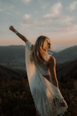 A woman standing confidently on a mountain peak at sunset.
