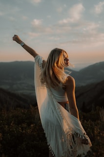 An inspiring woman standing confidently on a mountaintop at sunset.