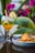 A refreshing drink garnished with lime and cinnamon sticks is placed on a polished surface next to a plate filled with folded tortilla chips. In the background, vibrant pink bougainvillea flowers and large green leaves add a tropical vibe.