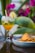A refreshing drink garnished with lime and cinnamon sticks is placed on a polished surface next to a plate filled with folded tortilla chips. In the background, vibrant pink bougainvillea flowers and large green leaves add a tropical vibe.