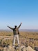 A smiling woman standing in a park, celebrating her fitness achievement with arms raised.