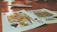 Playing cards are spread out on a wooden table, with the Queen and King of Spades prominently visible. The focus is on the vibrant colors and detailed designs of the cards, while other cards and hands are slightly blurred in the background, suggesting a game in progress.