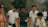 A group of young people is gathered outdoors in a rural area, surrounded by greenery. One person is holding a metallic container, and another holds a transparent plastic cup. They appear to be engaged in a conversation.