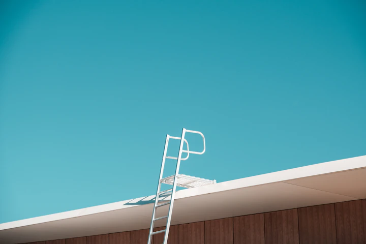 A ladder set against a roof edge for gutter cleaning