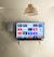 A modern living room features a wall-mounted flat-screen television displaying multiple streaming app icons, such as Apple TV, HBO Max, Netflix, Disney+, and Prime Video. Below the TV is a soundbar sitting on a small white shelf. A wicker pendant light hangs from the ceiling above, and the wall is painted a neutral color.