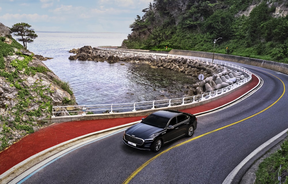 um carro preto dirigindo em uma estrada ao lado de um corpo de água