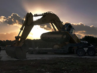 High-resolution photo of a heavy-duty excavator being loaded onto a transport truck at dusk.