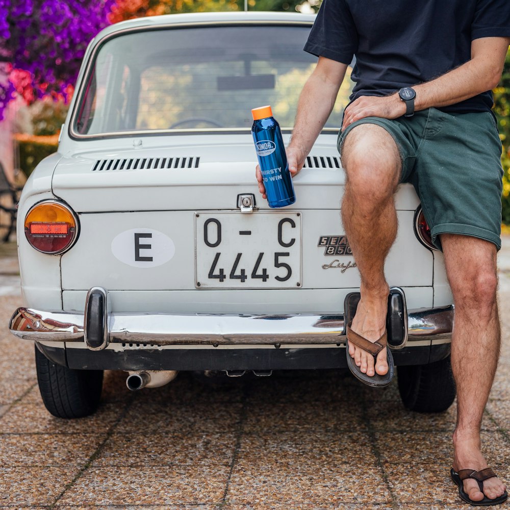 a man sitting on the back of a car with a can on the trunk