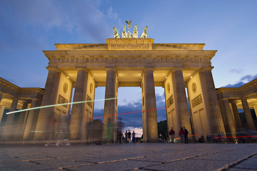 un gran arco dorado y azul con estatuas en la parte superior con la Puerta de Brandenburgo al fondo