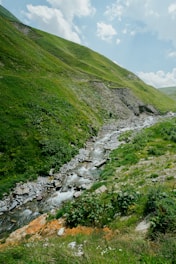 A serene winding sky-blue river flowing toward the viewer, framed by misty gray mountains with a bright yellow sun rising behind them.