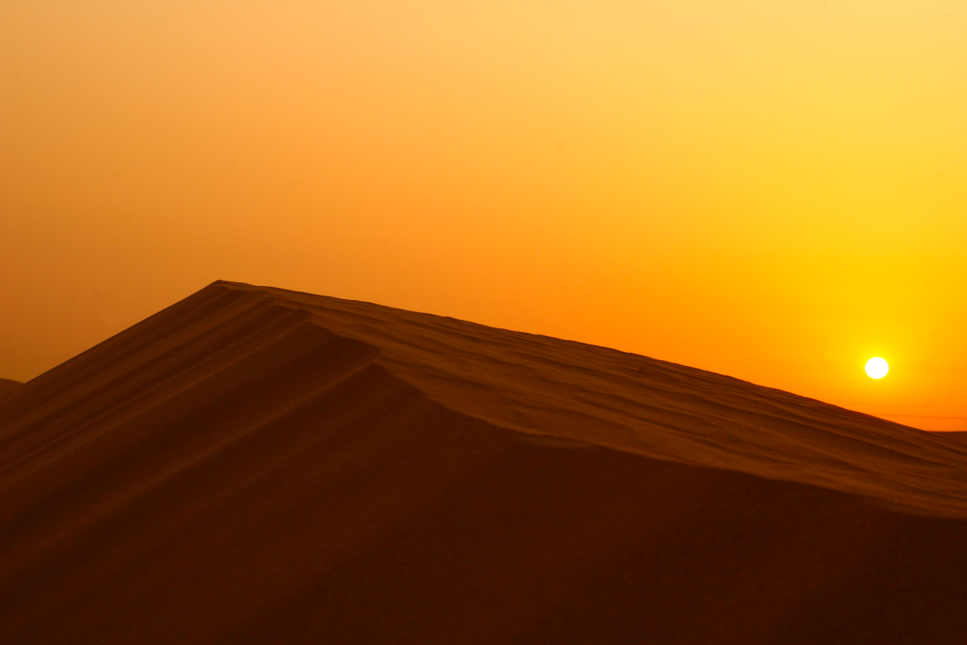 a large sand dune with the sun setting