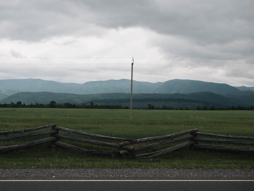 a field with a fence and a road with mountains in the background