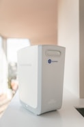 A modern reverse osmosis water filtration device, primarily white and gray in color, is placed on a clean, light-colored surface. The brand name 'Bluewater' and a blue circular button with an 'O' are visible on the front. The device has smooth and sleek contours, indicating a minimalist and contemporary design.