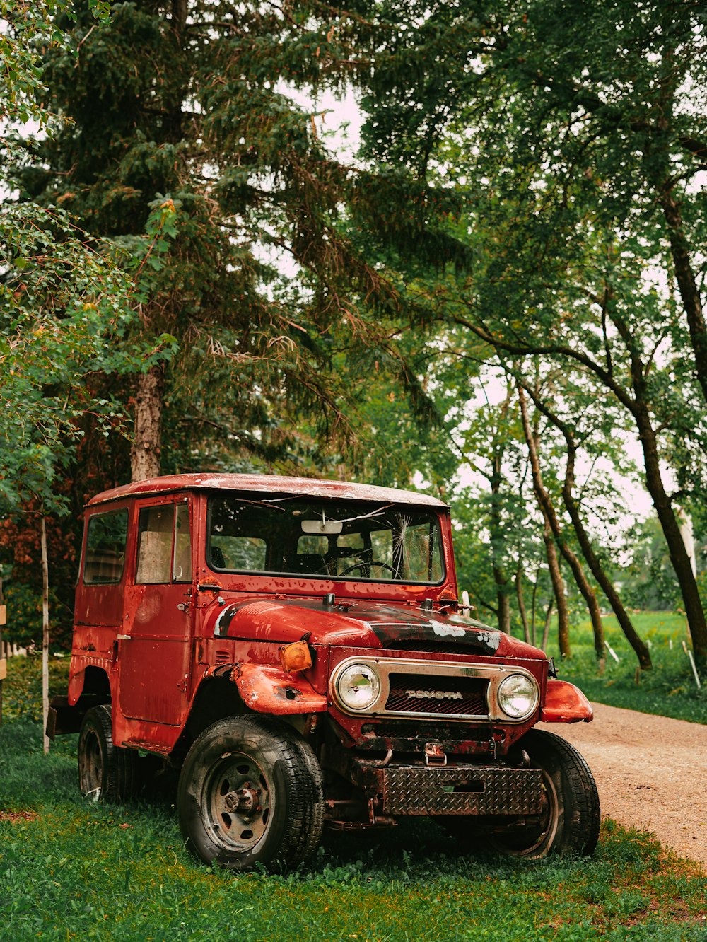 a red truck parked in a grassy area with trees in the back