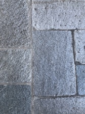 Rough, rectangular stone tiles arranged in a uniform pattern with visible grout lines in between. The surface texture appears grainy and the stones have a mixture of light and dark gray tones.