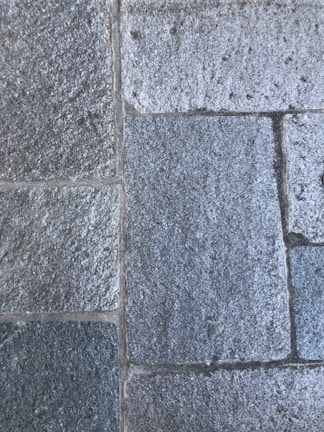Rough, rectangular stone tiles arranged in a uniform pattern with visible grout lines in between. The surface texture appears grainy and the stones have a mixture of light and dark gray tones.