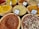 Various types of spices are displayed in wooden bowls, each labeled with their names. The spices include vibrant colors such as yellow, red, and mixtures of different spices. The labels identify them as Falafel Spice, Fish Spice, Harissa Spice, and Mixed Pepper, among others.