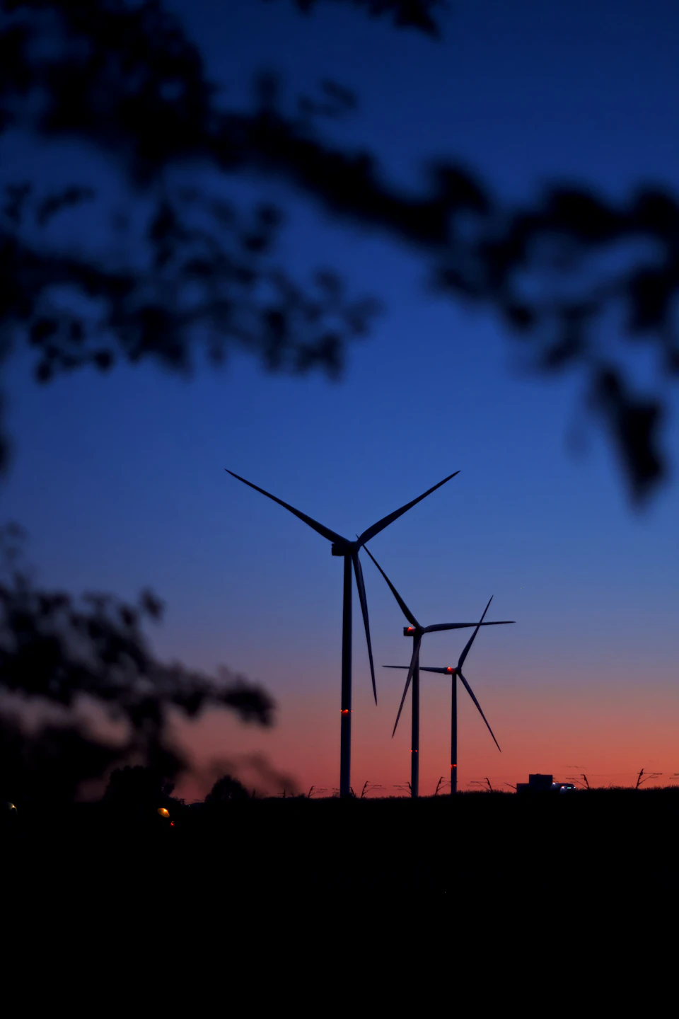 Two wind turbines stand tall against a dark blue sky with orange and pink hues