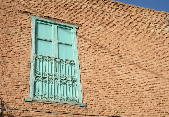 A turquoise window in a wall of patterned yellow brick — Tozeur, Tunisia