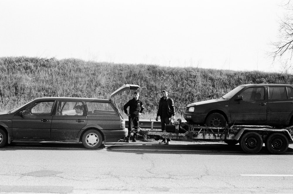 a couple of men standing next to a couple of cars with surfboards