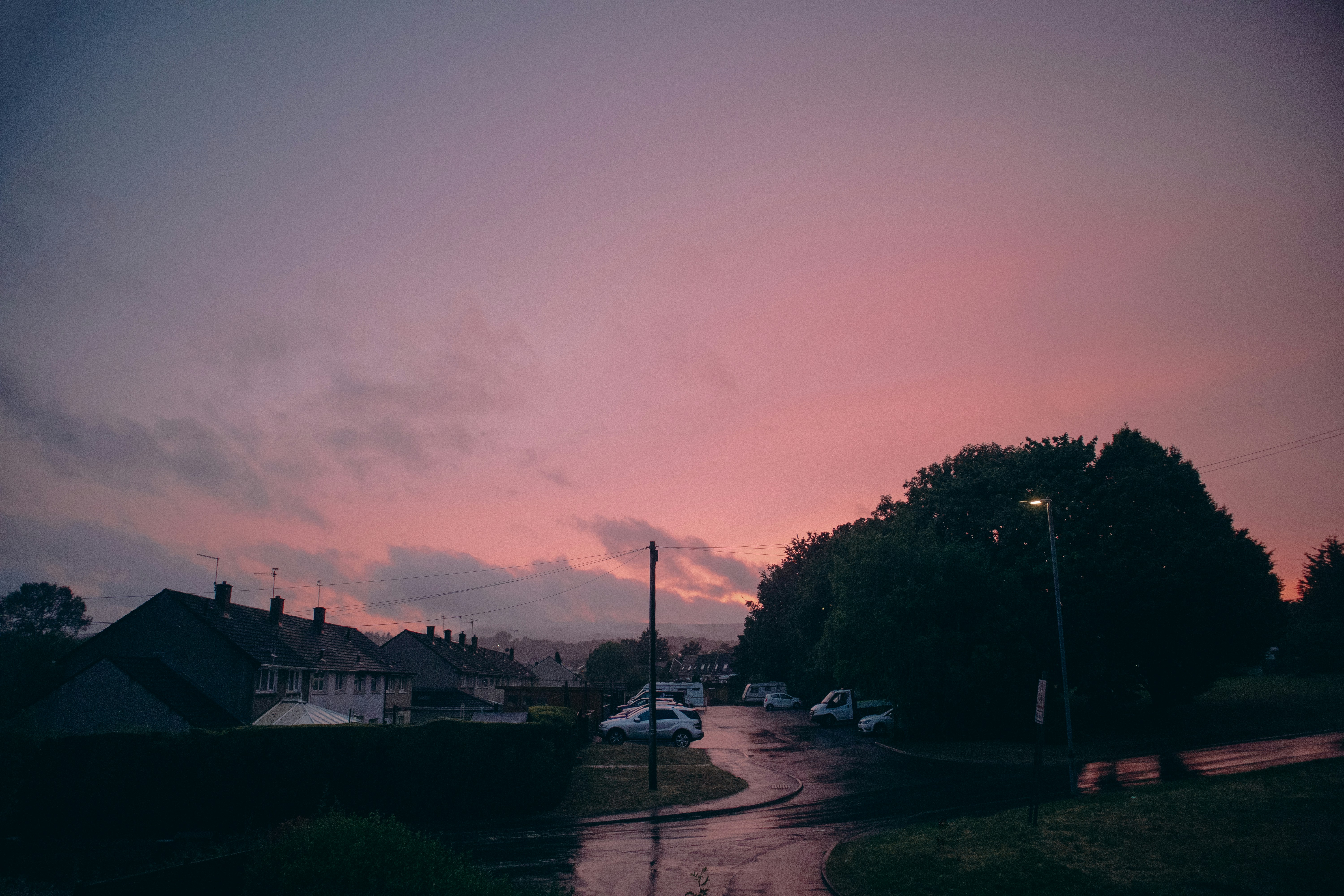 a street with cars parked on the side and a pink and purple sky