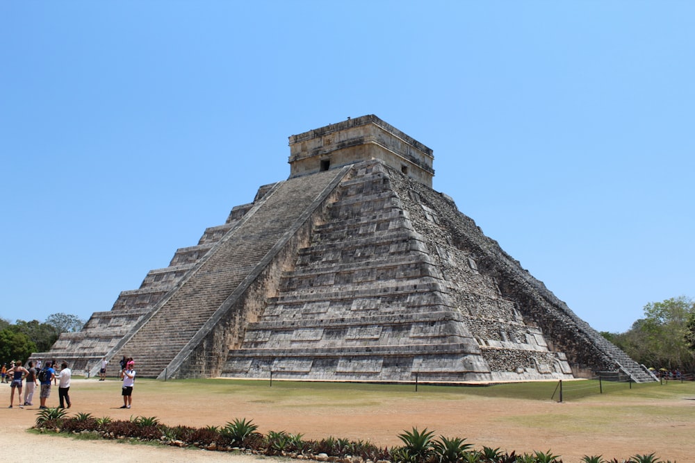 una piramide con persone in piedi di fronte ad essa con Chichen Itza sullo sfondo