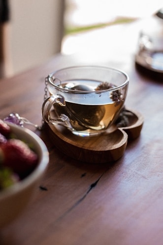 Heart-shaped reusable tea infuser resting on a wooden tray with loose herbal leaves