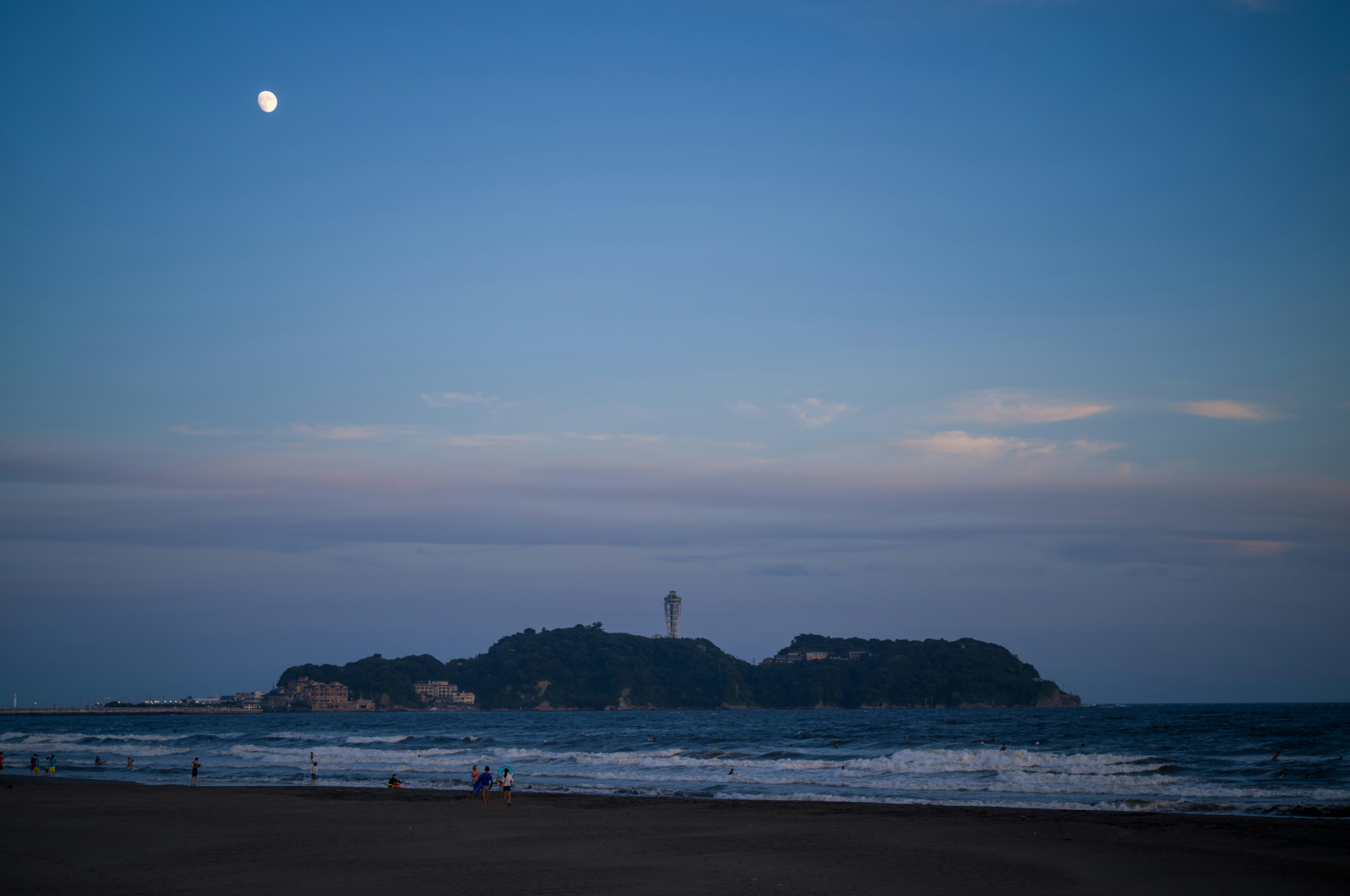 a beach with people and a lighthouse in the distance