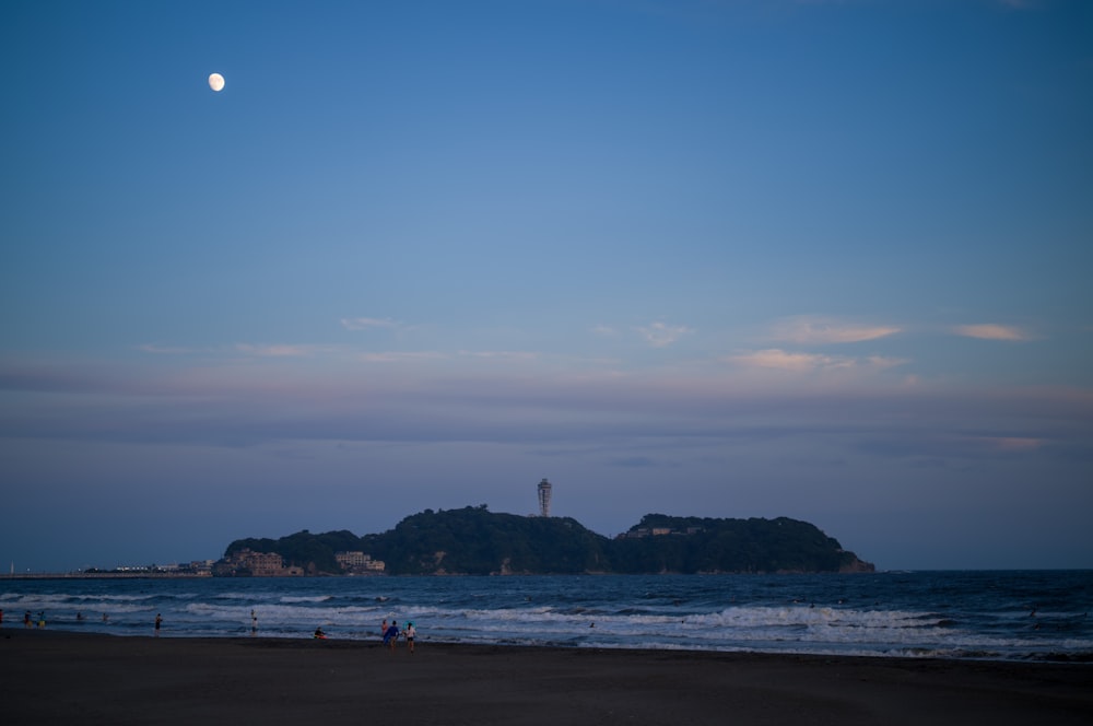 a beach with people and a lighthouse in the distance