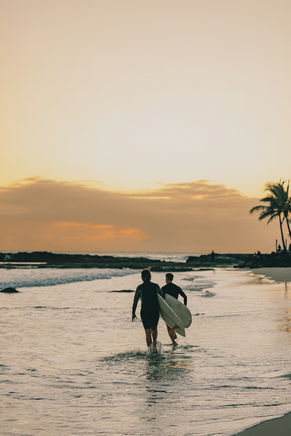 a couple of people walk across the water with surfboards