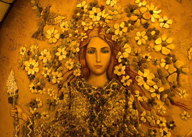 A mosaic of a woman surrounded by vibrant flowers, intricately crafted with stones and earthy materials. She holds a flower in her hands, and her serene expression conveys a sense of calm and beauty.