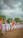A group of people dressed in white uniforms are marching on a dirt ground holding Indian flags. The background features lush green trees under a cloudy sky.