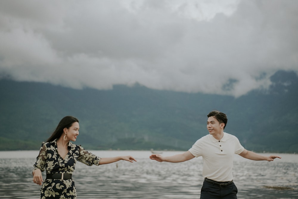 a man and woman holding hands and standing in front of water