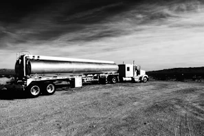 A black gold branded tanker truck parked at an industrial site during sunrise.