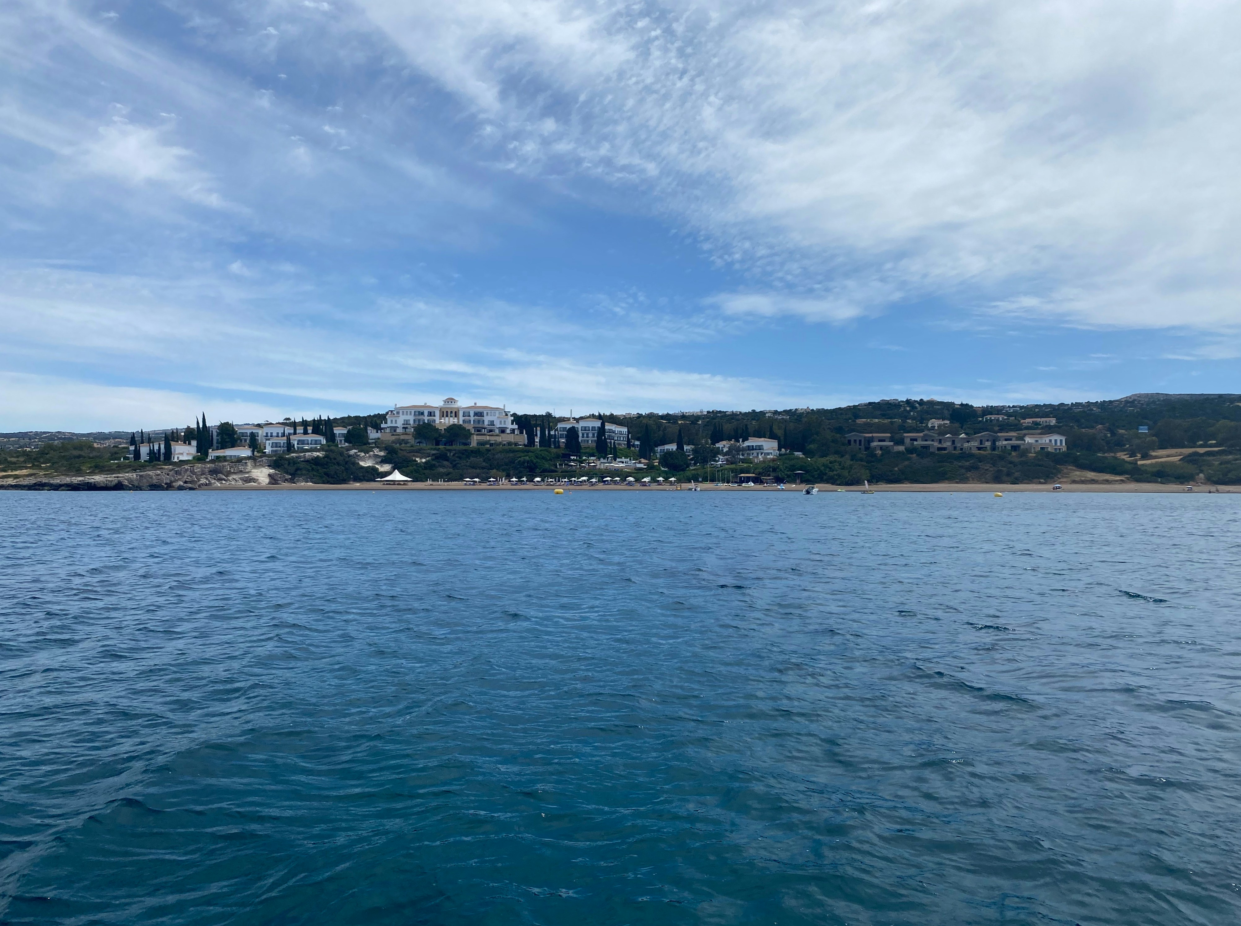 a body of water with buildings in the background, A serene moment in the waters of Chrysochou Bay, Neo Chorio, Cyprus