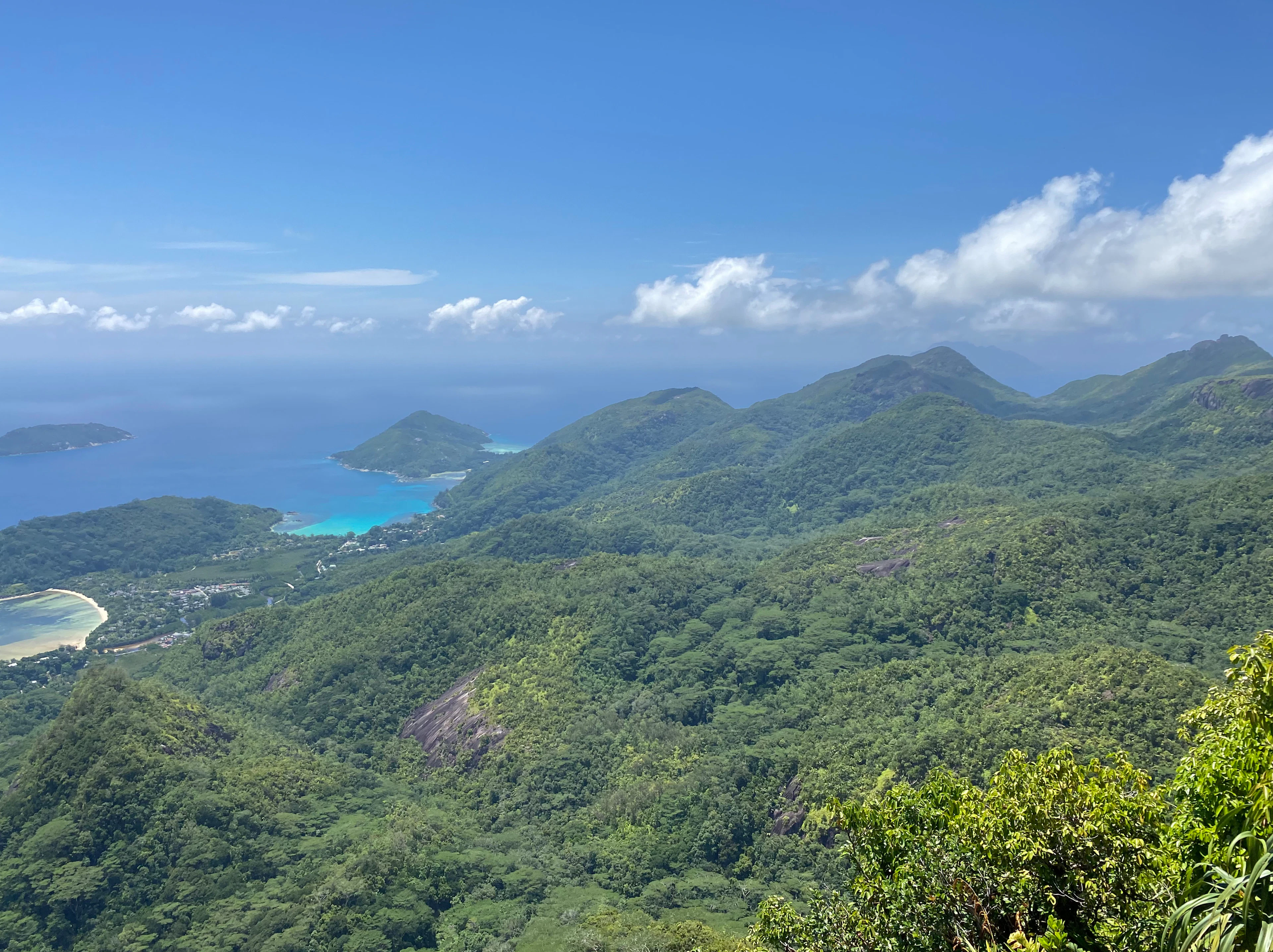 The forested ridges of Morne Seychellois National Park on Mahe falling away to turquoise bays and offshore islands under a bright sky.