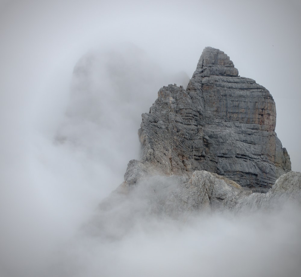 a tall rock formation with clouds around it
